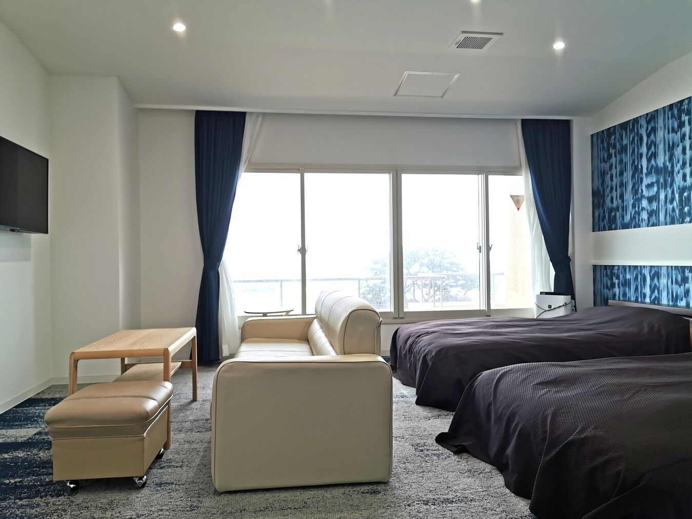 A modern hotel room with a sofa, a small table, a bed, and a TV.