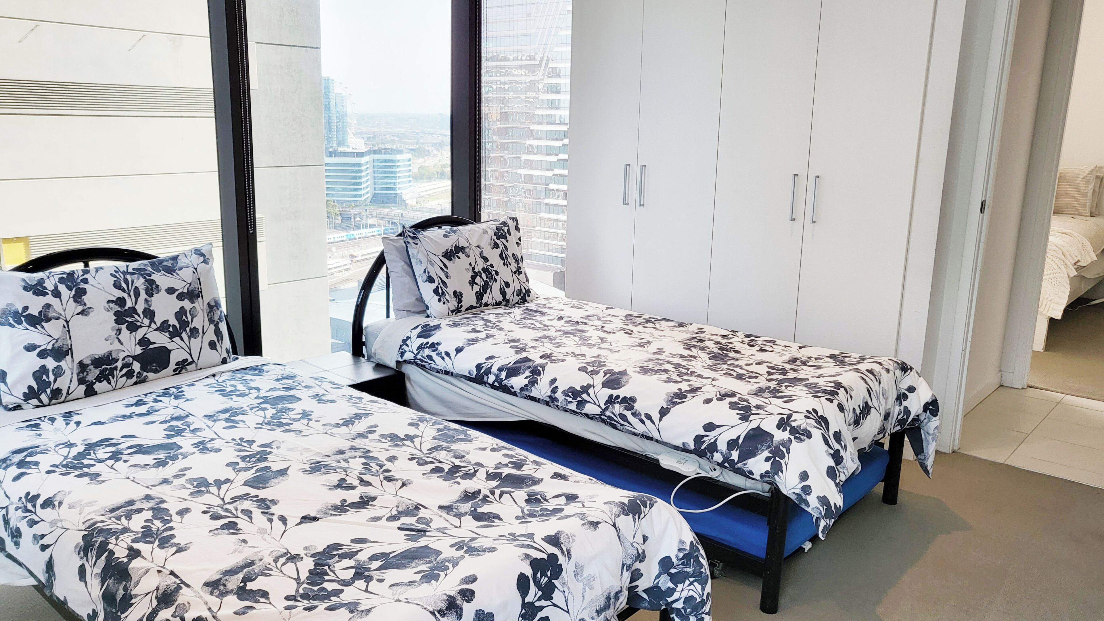 A modern bedroom with two beds, a wardrobe, and a city view.