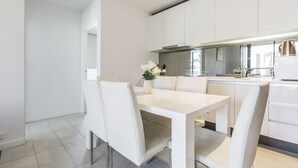 A modern kitchen with white cabinetry, a dining table with chairs, and a vase with flowers. - C3CBD Melbourne Apartment (Melbourne)