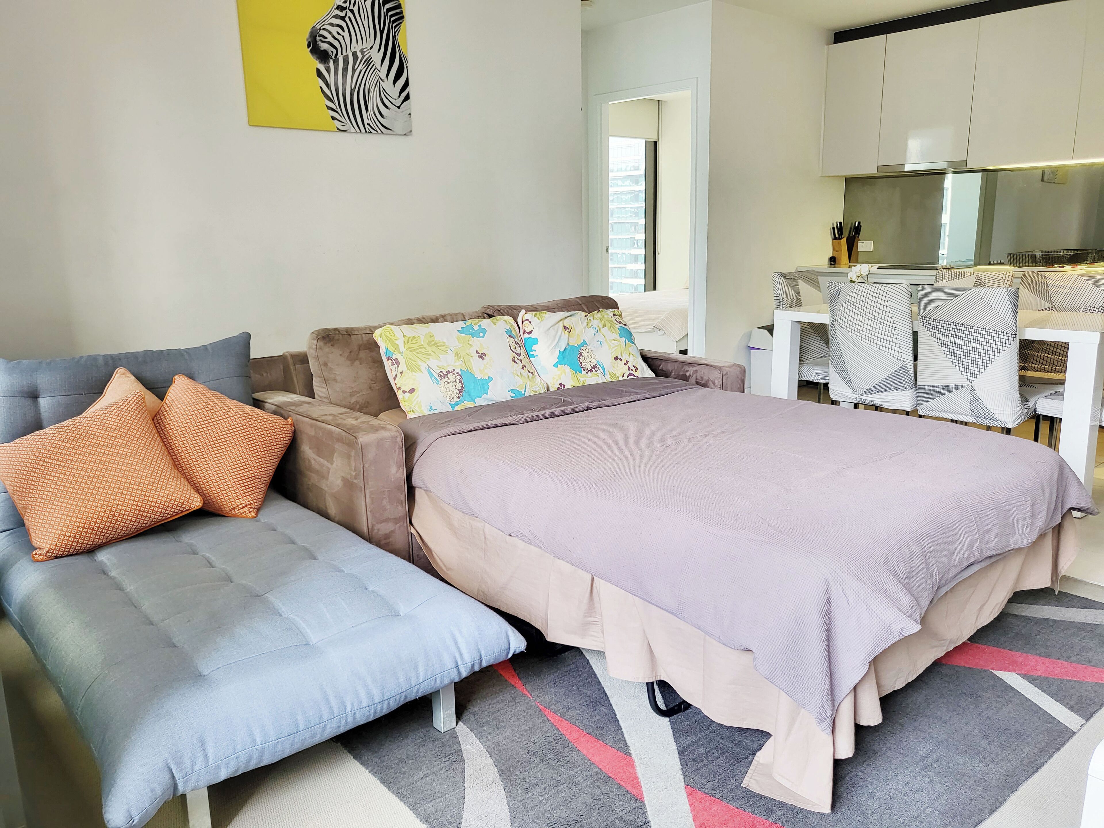 A modern bedroom with a sofa, a bed with a patterned bedspread, and a zebra artwork on the wall.