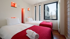 A hotel room with two beds, red and white bedding, a large window, and a view of buildings outside. - Udelka A (Kutchan)