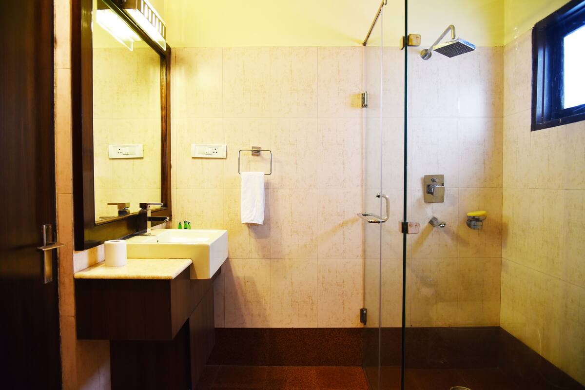 Un baño con cabina de ducha de vidrio, un lavamanos con espejo y una toalla colgada en la pared.