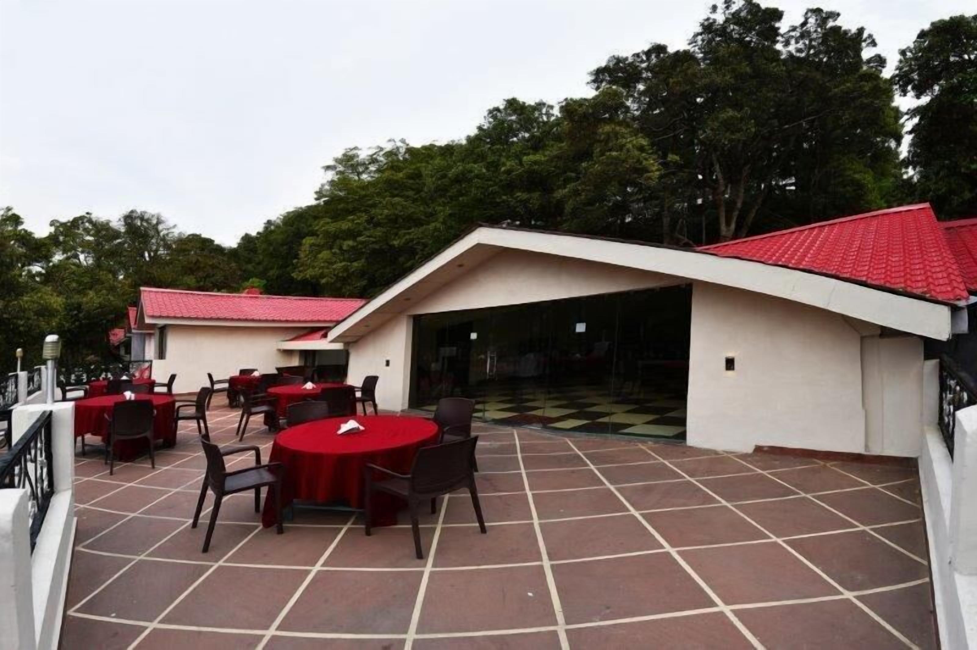 Un patio al aire libre con mesas y sillas redondas, una zona de estar cubierta y vistas a árboles.