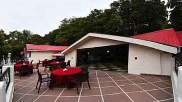 Un patio al aire libre con mesas y sillas redondas, una zona de estar cubierta y vistas a árboles.