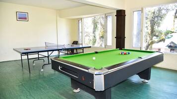 A pool table with a green felt surface, a table tennis table, and a framed picture on the wall.