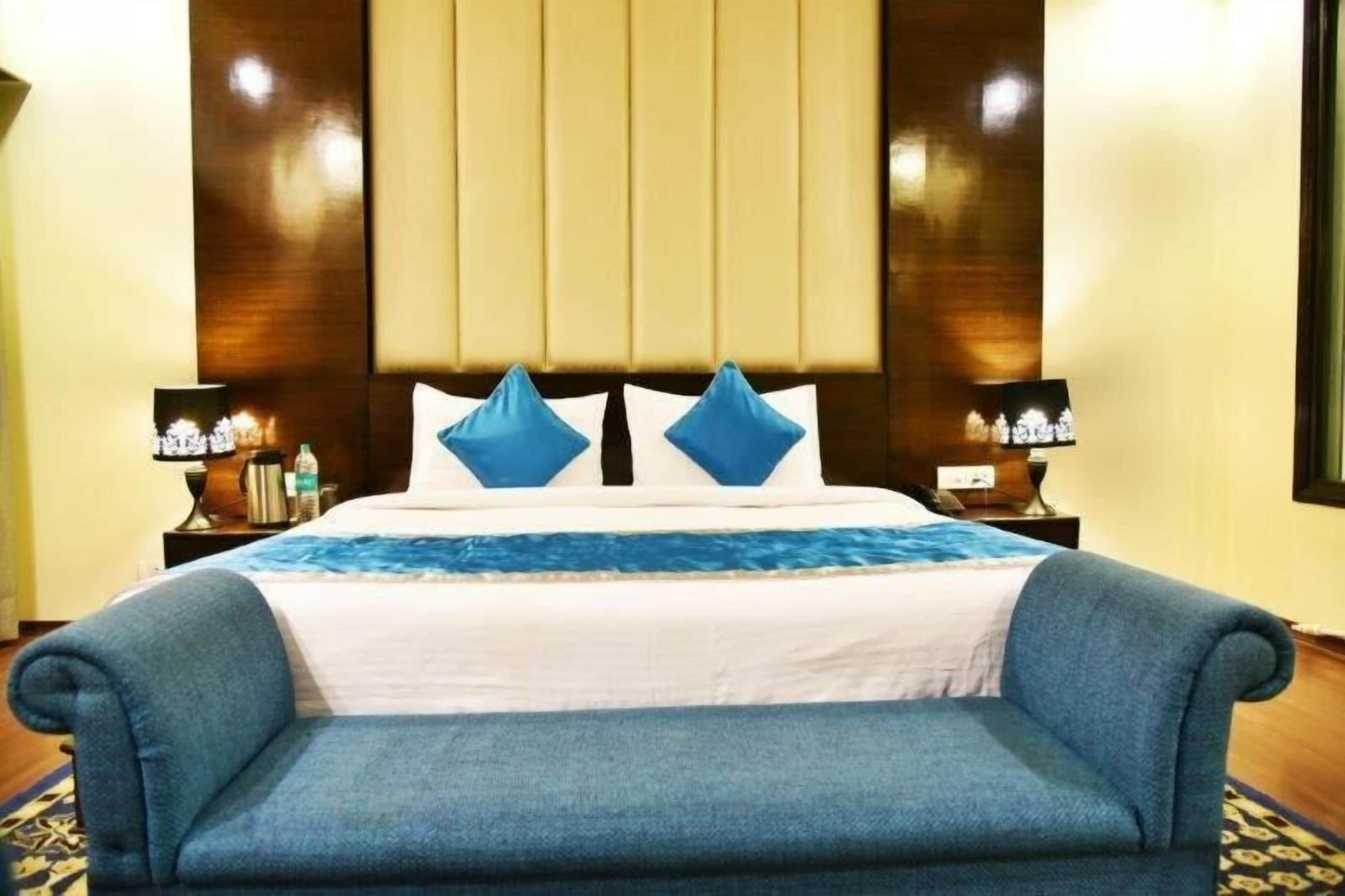 A hotel room with a large bed, two bedside tables with lamps, a blue sofa, and a patterned rug.