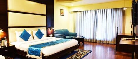 A hotel room with a large bed, a sofa, a desk, and a TV.