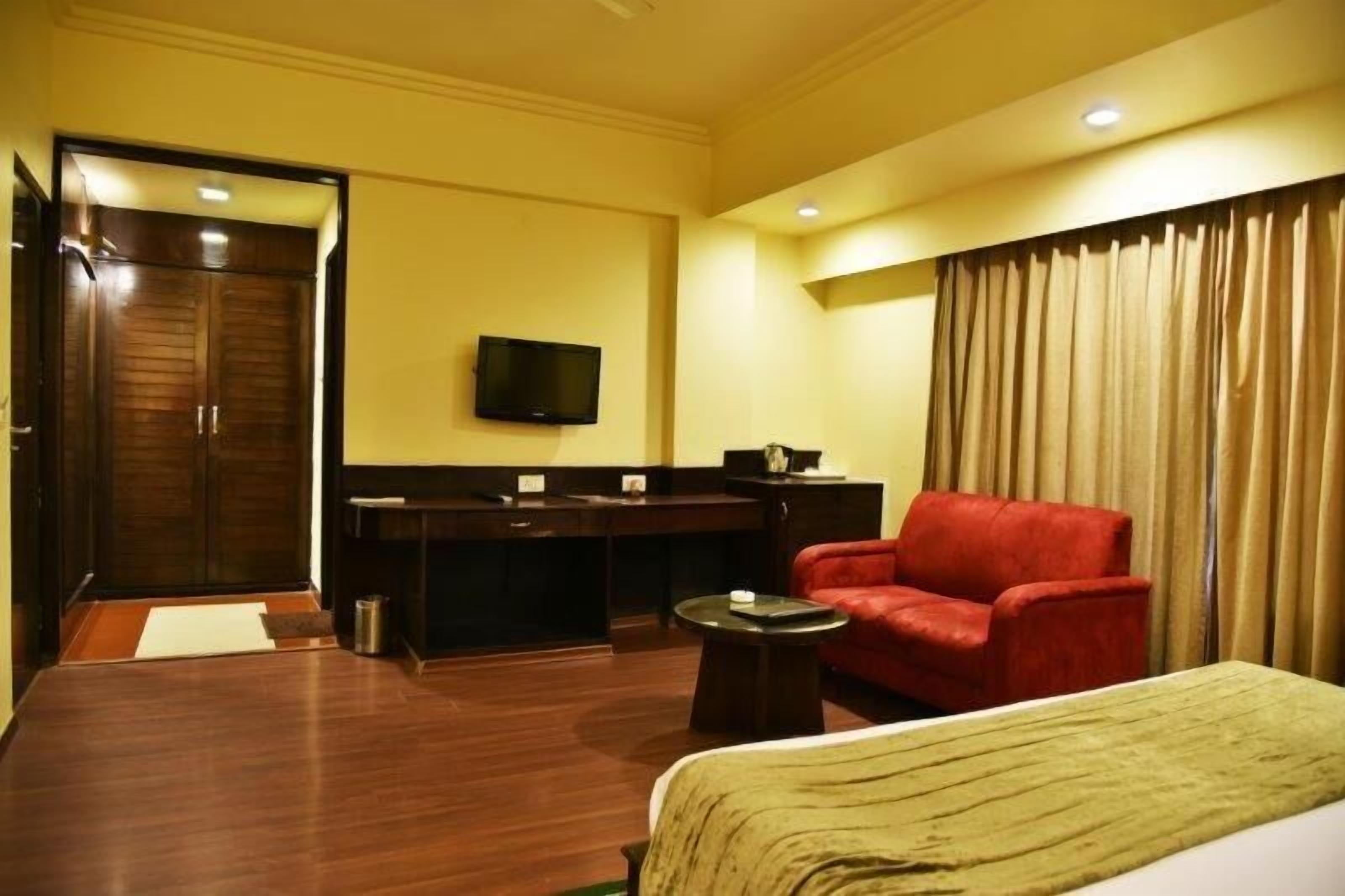 A hotel room with a bed, a red armchair, a desk with a television, and a curtain.