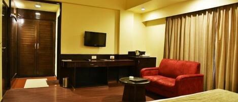 A hotel room with a bed, a red armchair, a desk with a television, and a curtain.