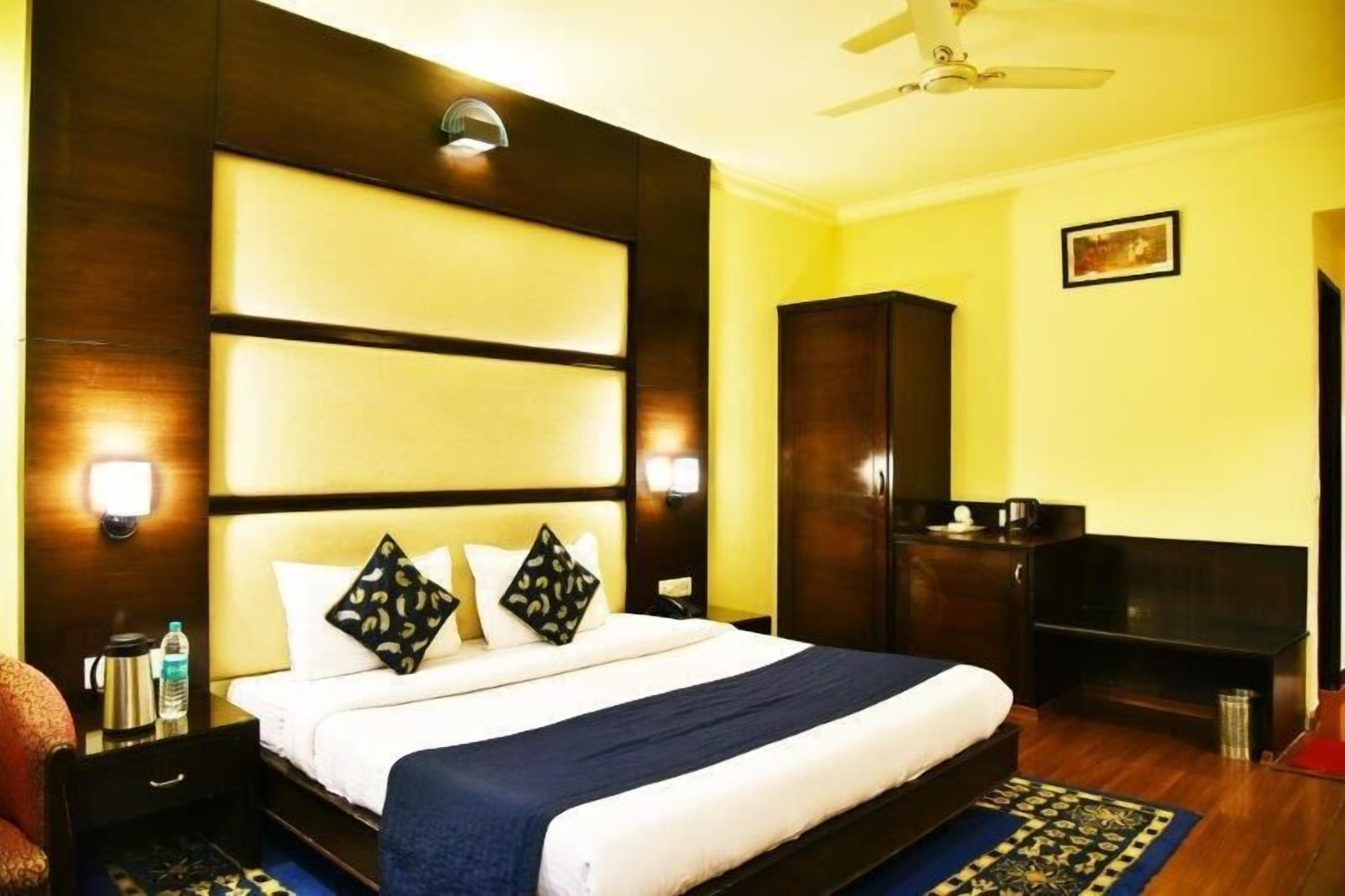 A hotel room with a large bed, wooden headboard, bedside lamps, a wardrobe, and a ceiling fan.