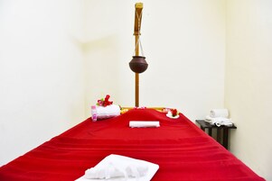 Una stanza spa con un lettino da massaggio rosso, un utensile di legno per massaggi e asciugamani.