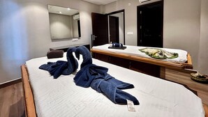 A hotel room with a bed, a wooden headboard, a bedside table with a tray, a mirror, and an air conditioning unit.