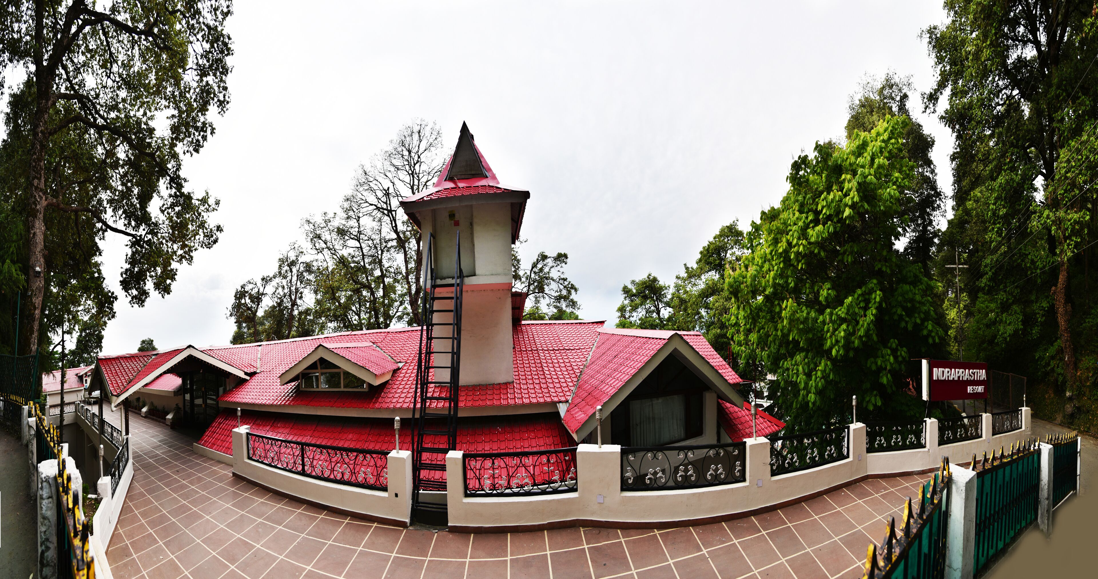 A building with a red roof and a tower, surrounded by a fence and trees.