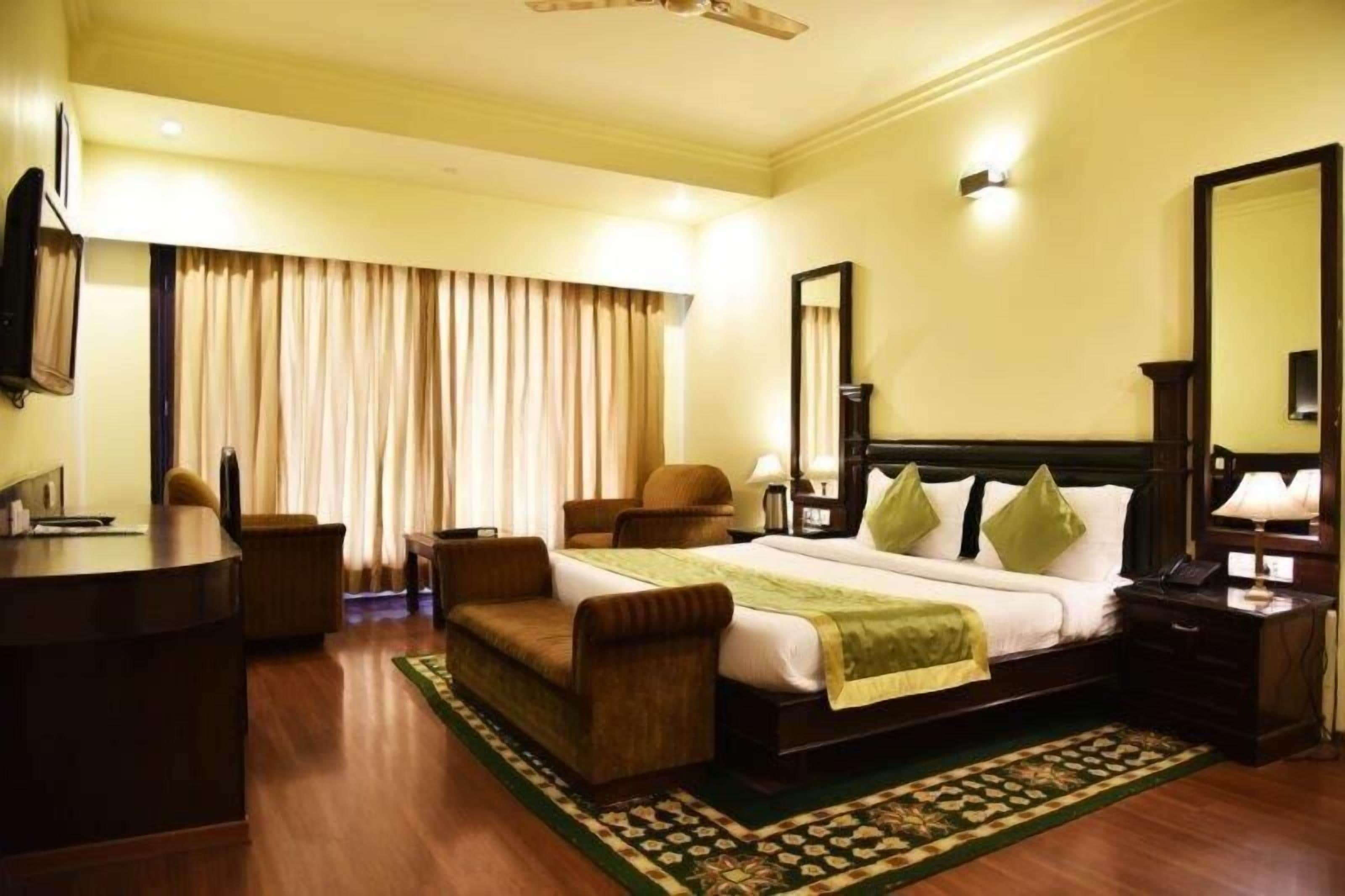A hotel room with a bed, a desk, a chair, a mirror, and curtains.