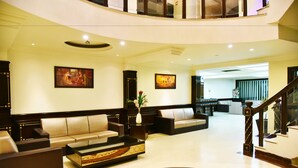 A spacious lobby with a curved staircase, leather sofas, a coffee table, and artwork on the walls.