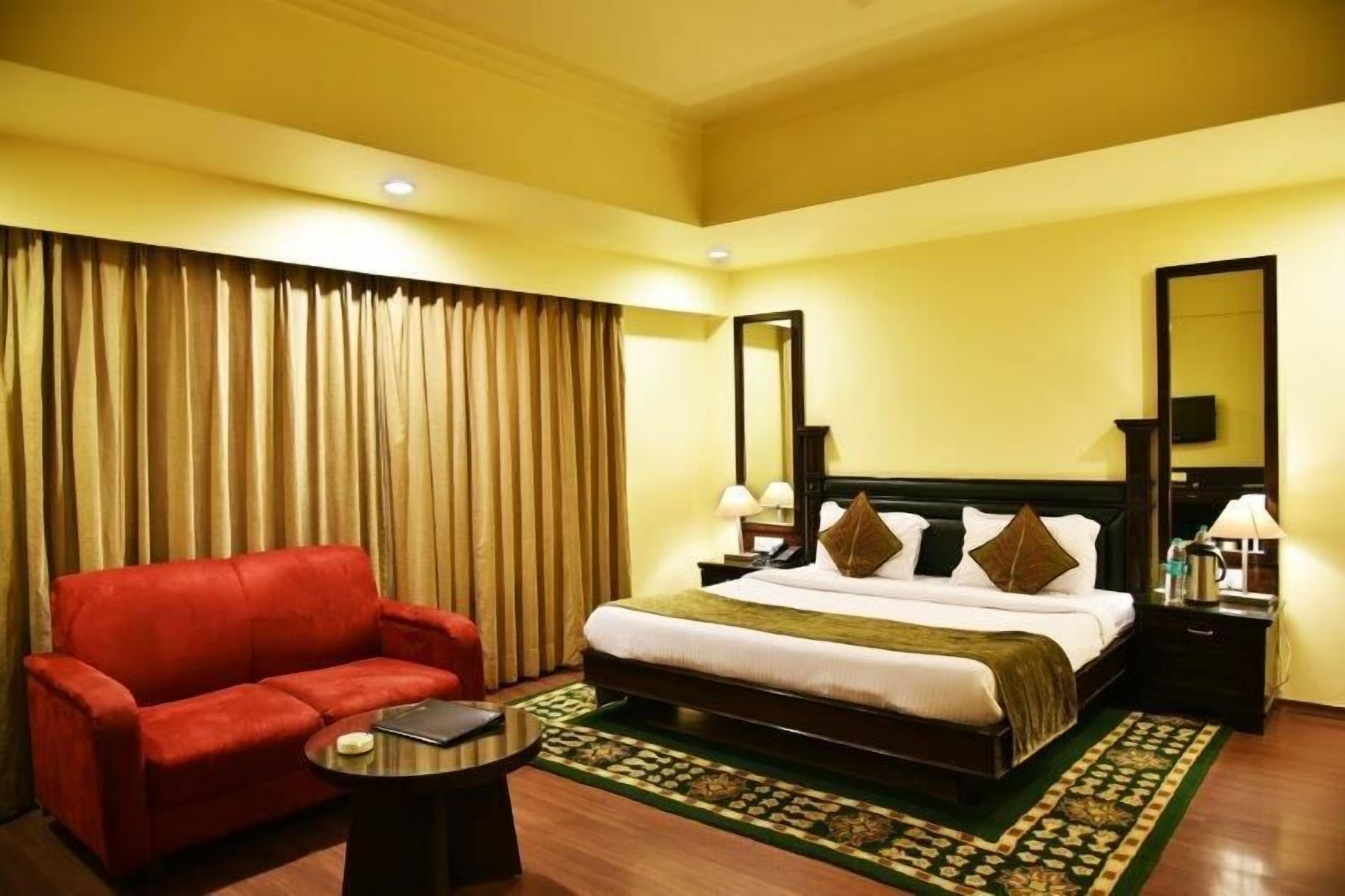 A hotel room with a large bed, a red sofa, a small table, and a patterned rug.