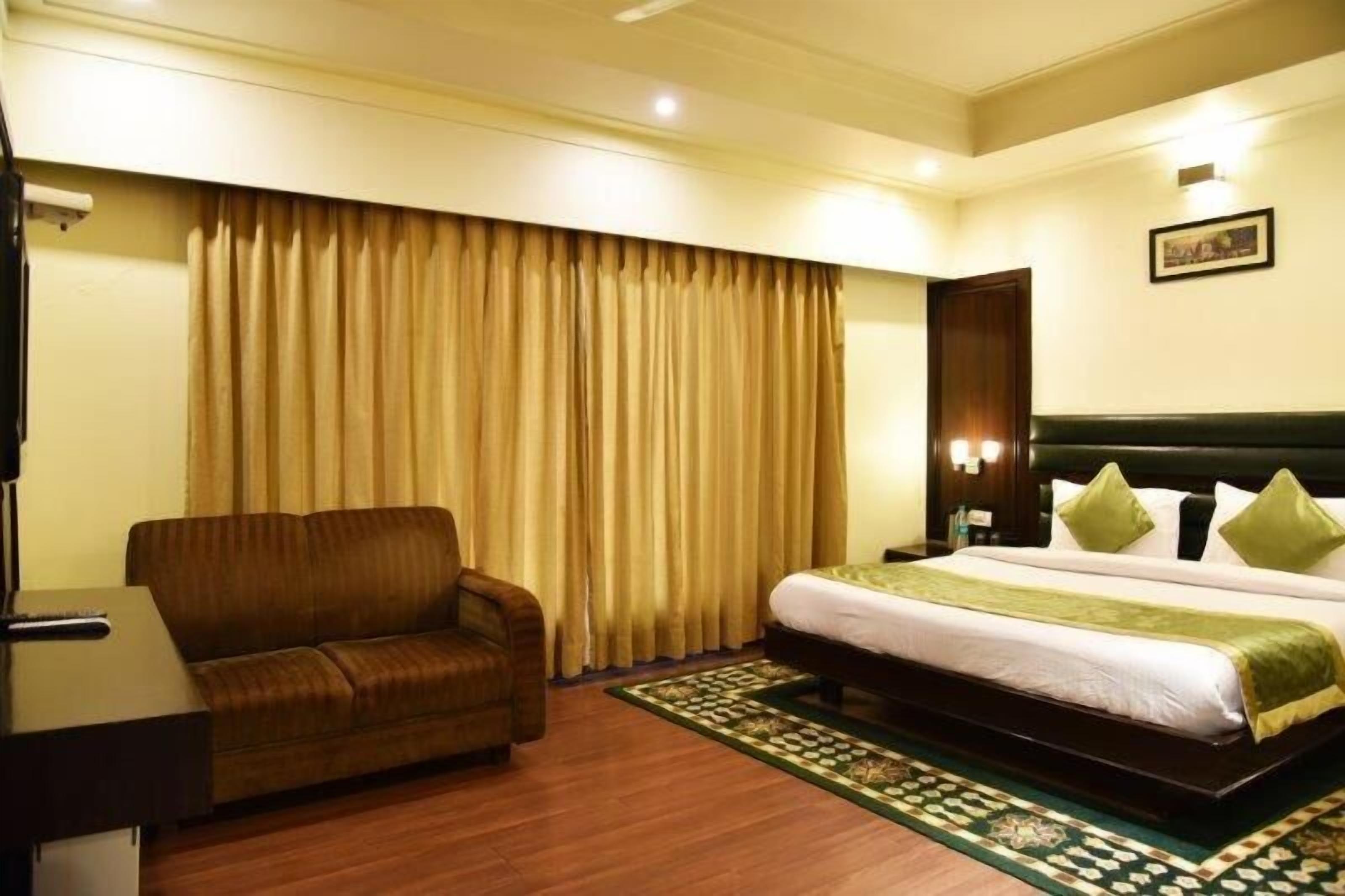 A hotel room with a bed, a sofa, a desk, and a large window with curtains.