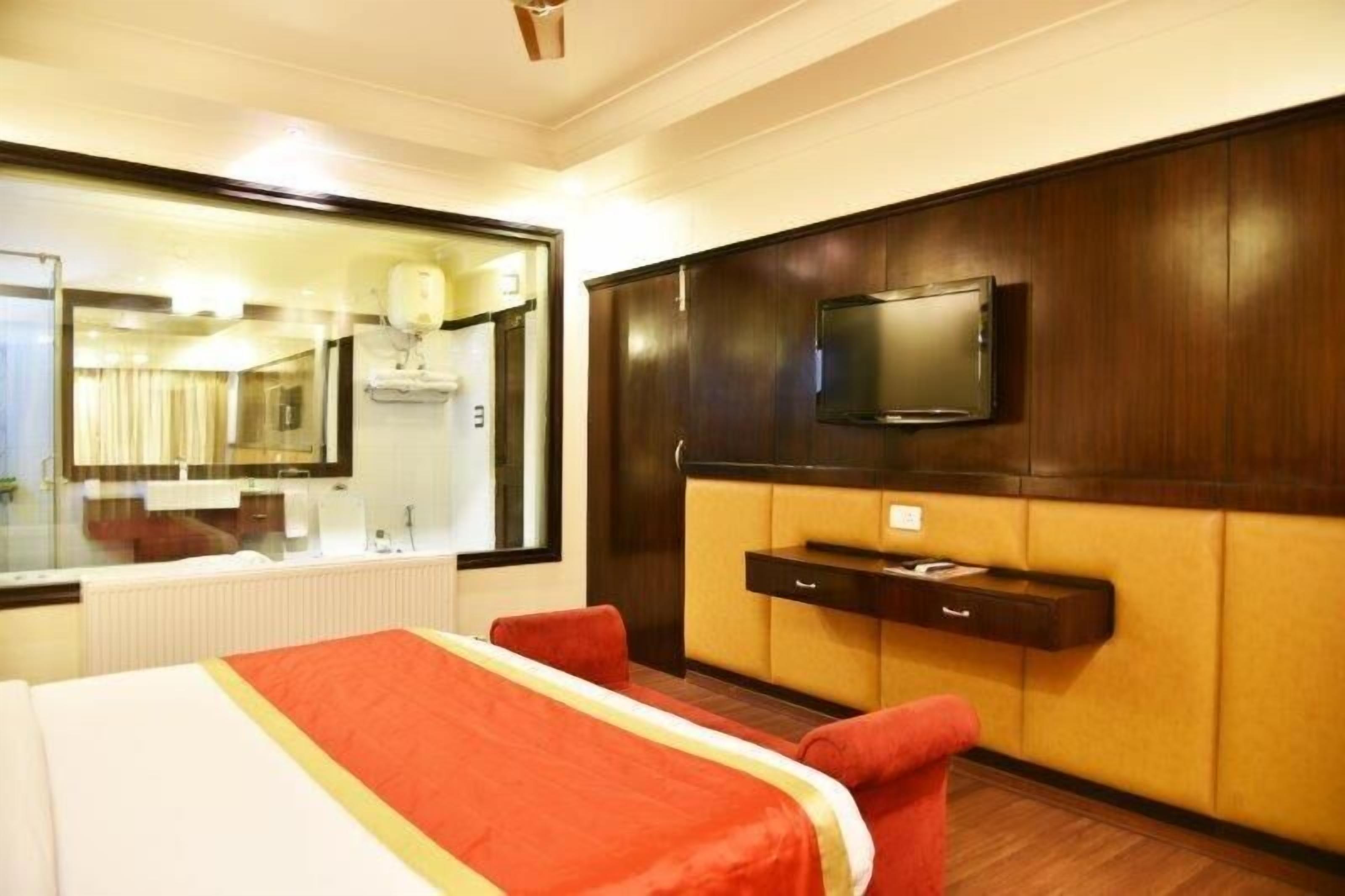 Habitación de hotel con cama, televisión montada en la pared, espejo y ventana.