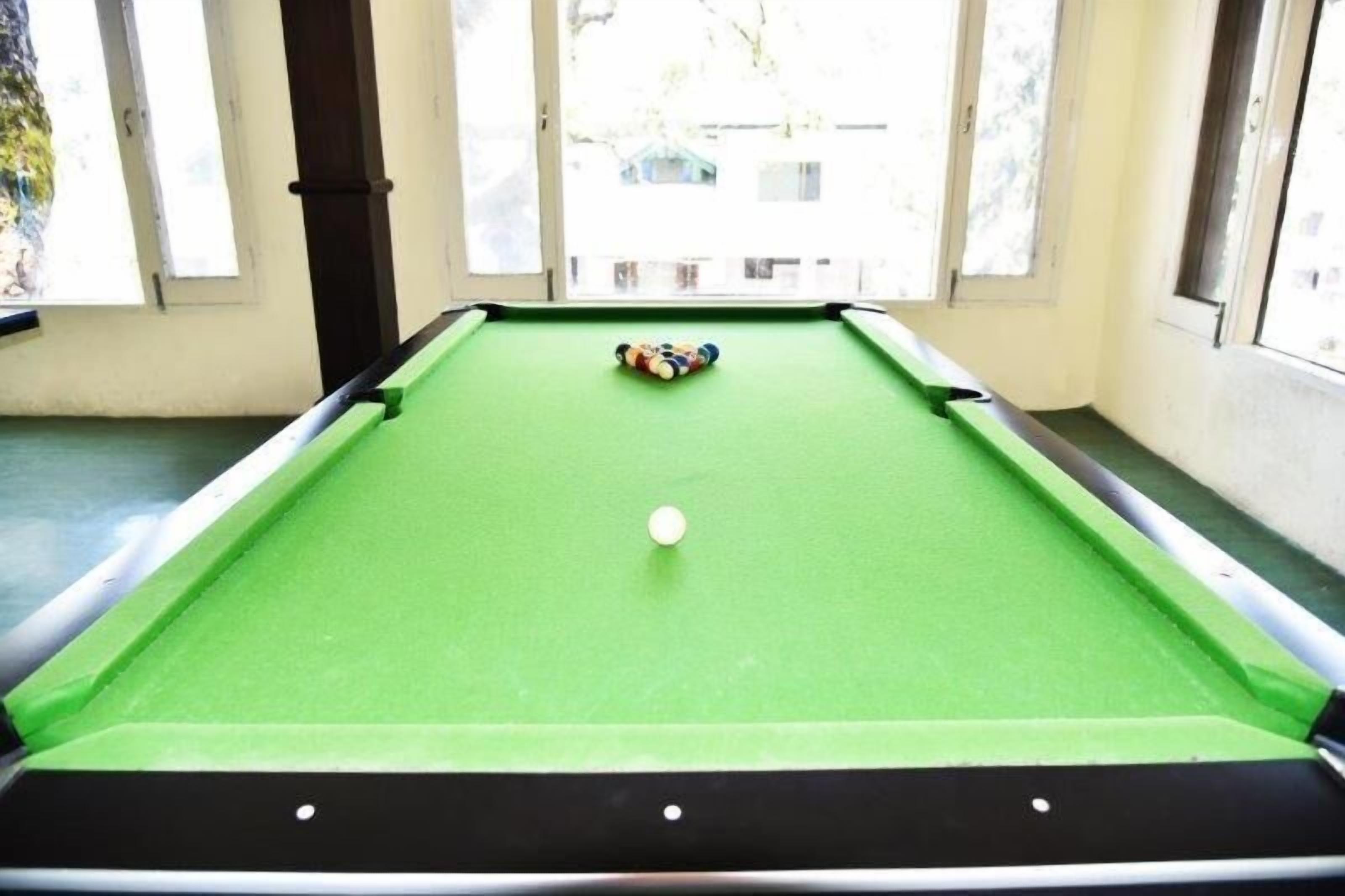Une table de billard recouverte d’un drap vert, avec une bille blanche et un jeu de billes de différentes couleurs au centre.