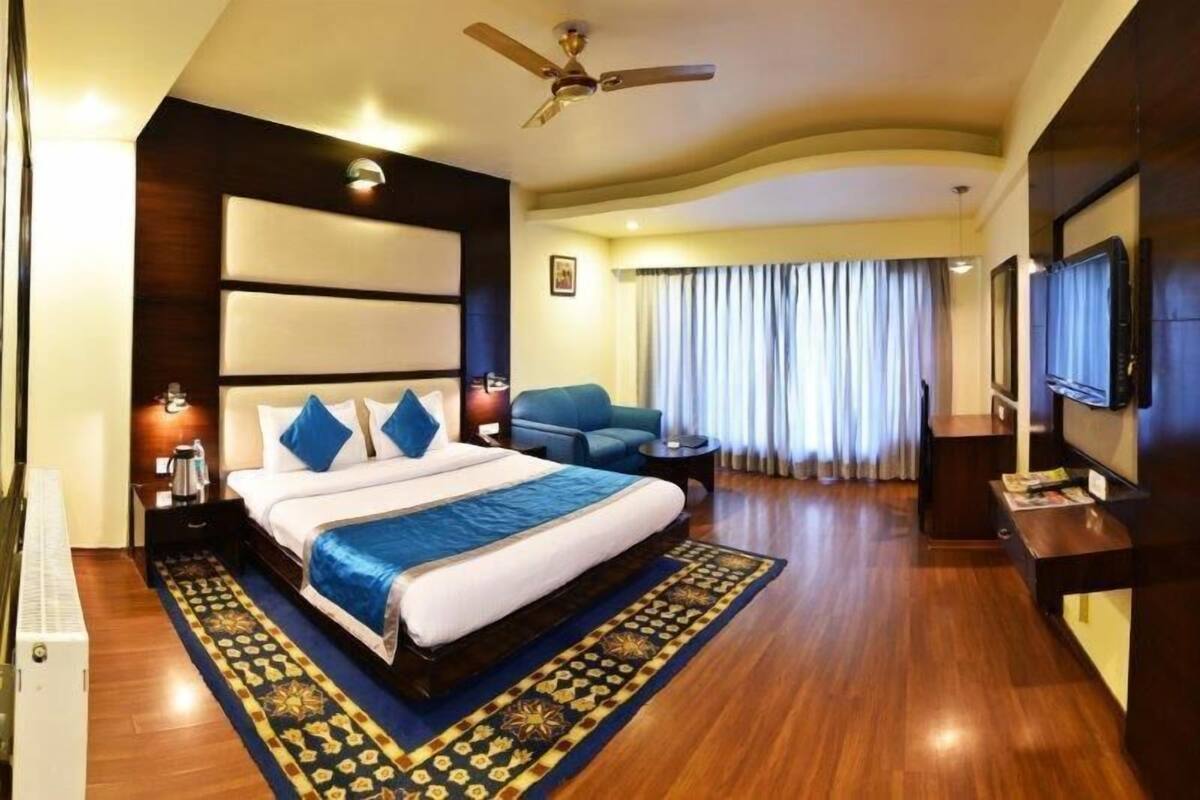 Habitación de hotel con una cama grande, ventilador de techo, televisor y un área de descanso con cortinas.