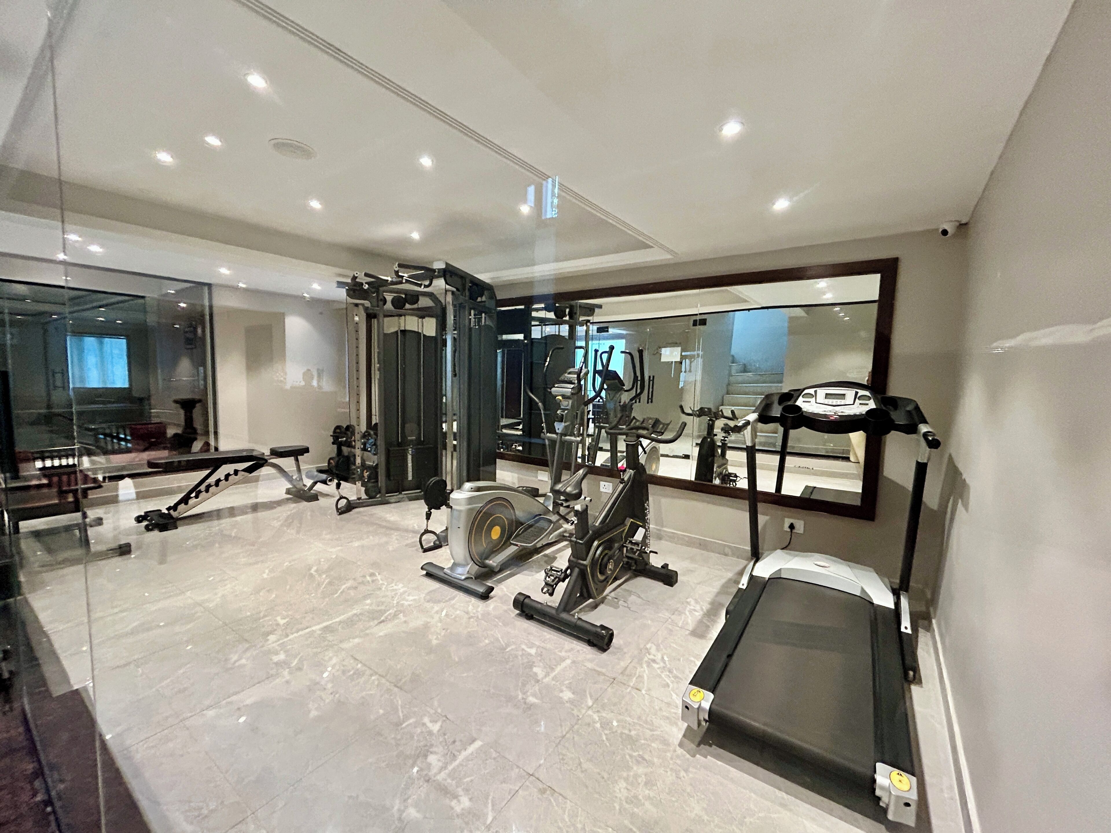 A modern gym with various exercise equipment, a large mirror, and a marble floor.