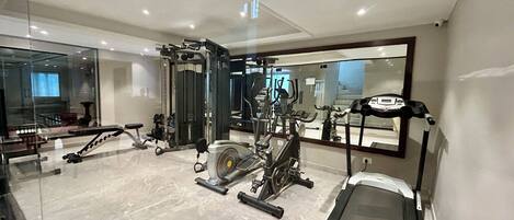 A modern gym with various exercise equipment, a large mirror, and a marble floor.