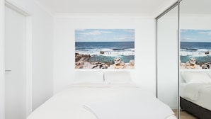 Una camera da letto con un letto grande, vista sull'oceano attraverso una finestra e uno specchio che riflette l'ambiente.