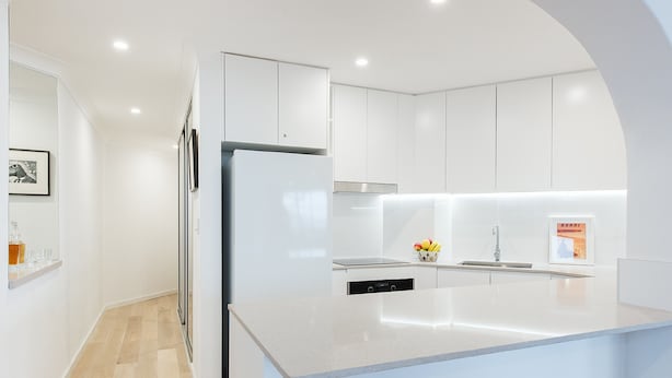 Una cucina moderna con mobili bianchi, un frigorifero integrato e un'isola centrale con lavello.