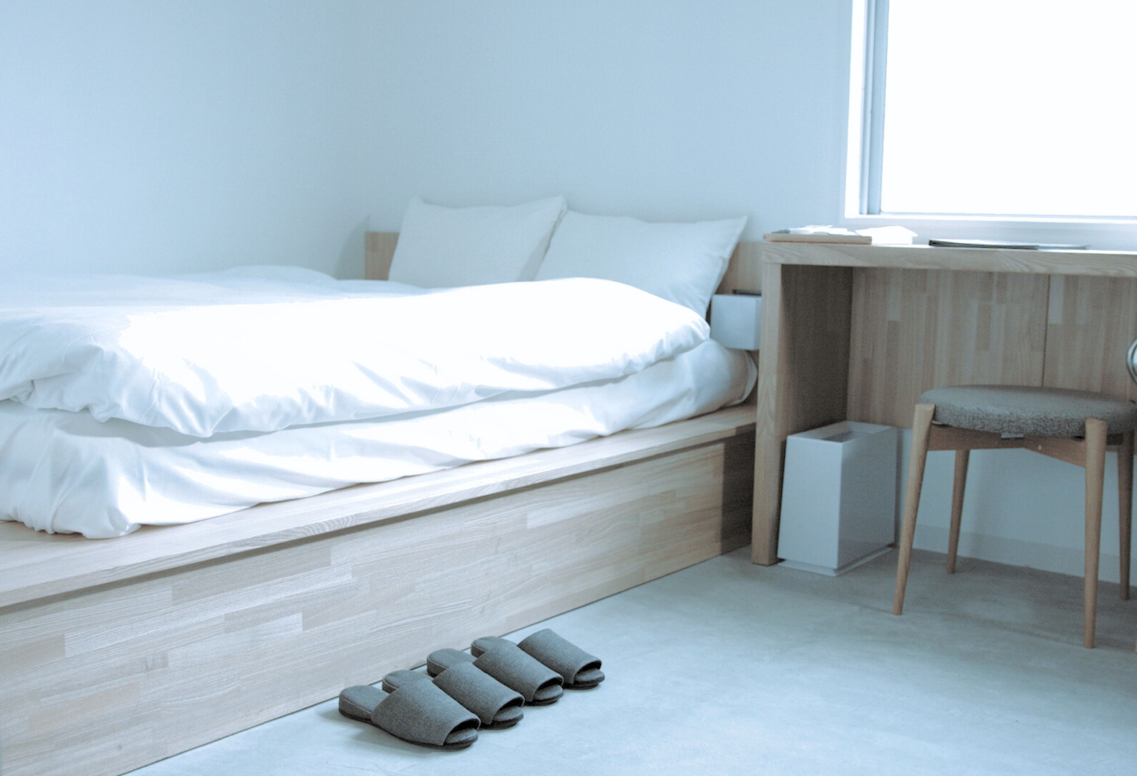 Een minimalistische slaapkamer met een bed, bureau en stoel.