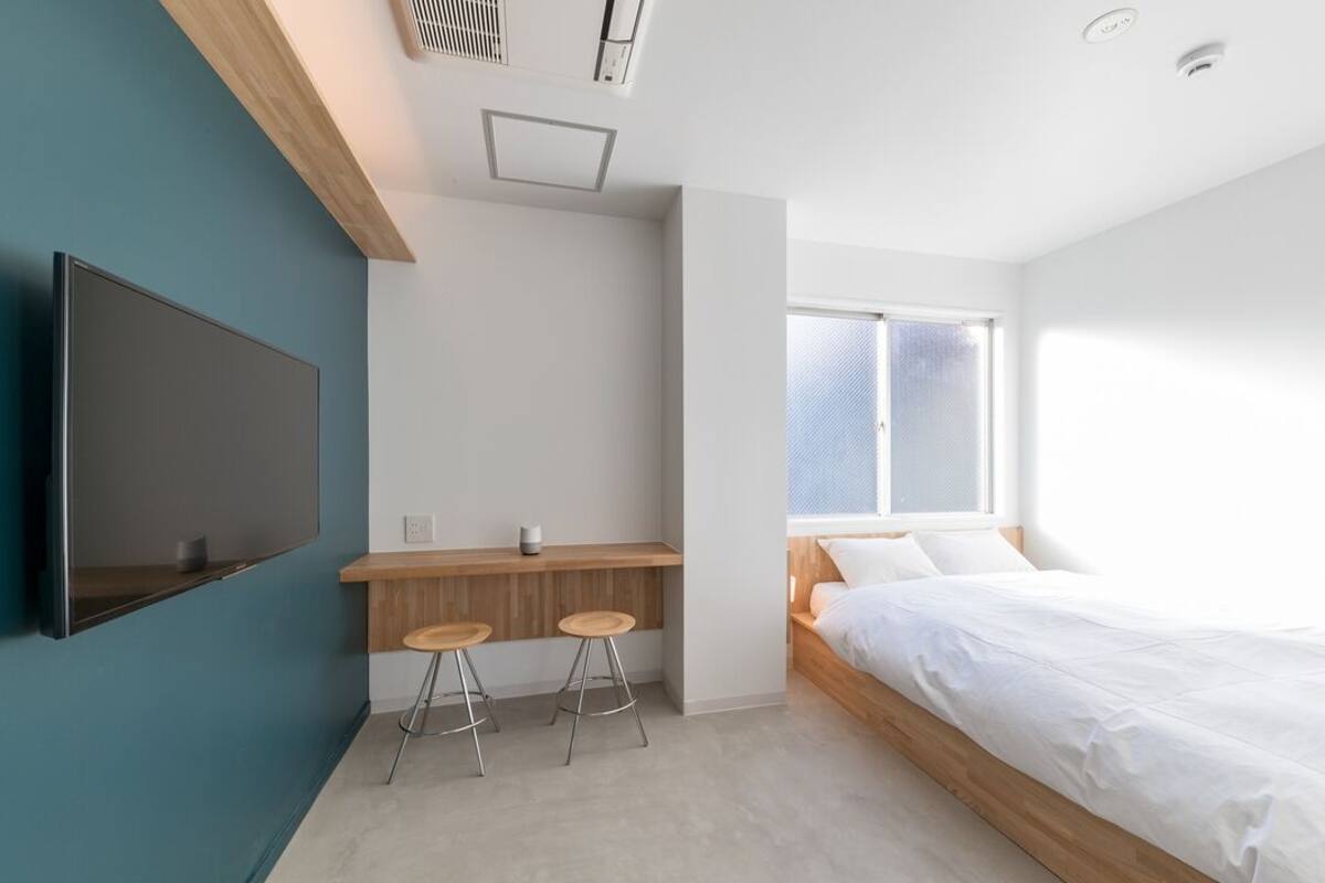 A modern bedroom with a bed, a TV mounted on the wall, and a desk with stools.