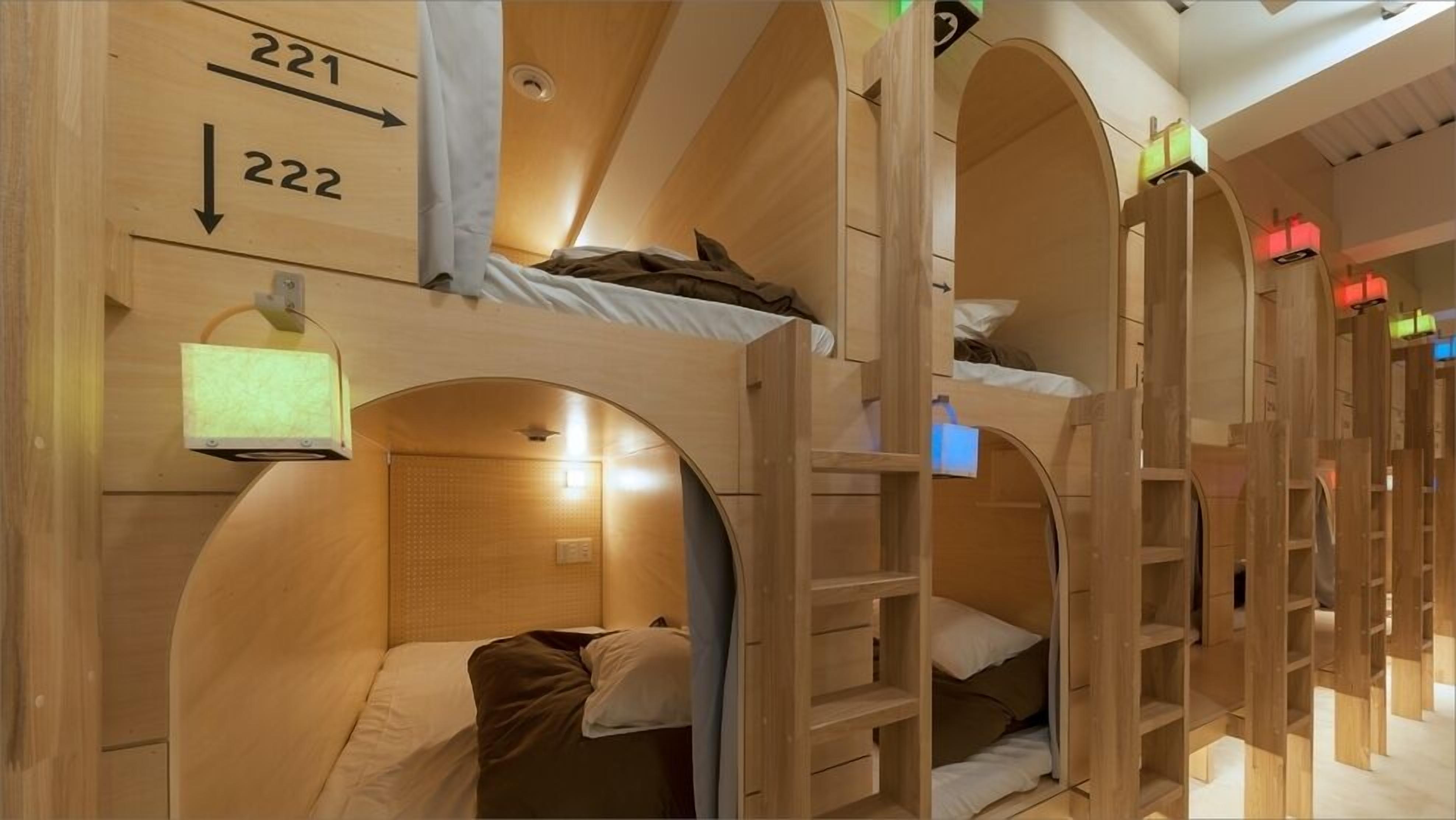 A row of bunk beds with wooden arches, a small shelf, and a wall-mounted light fixture.