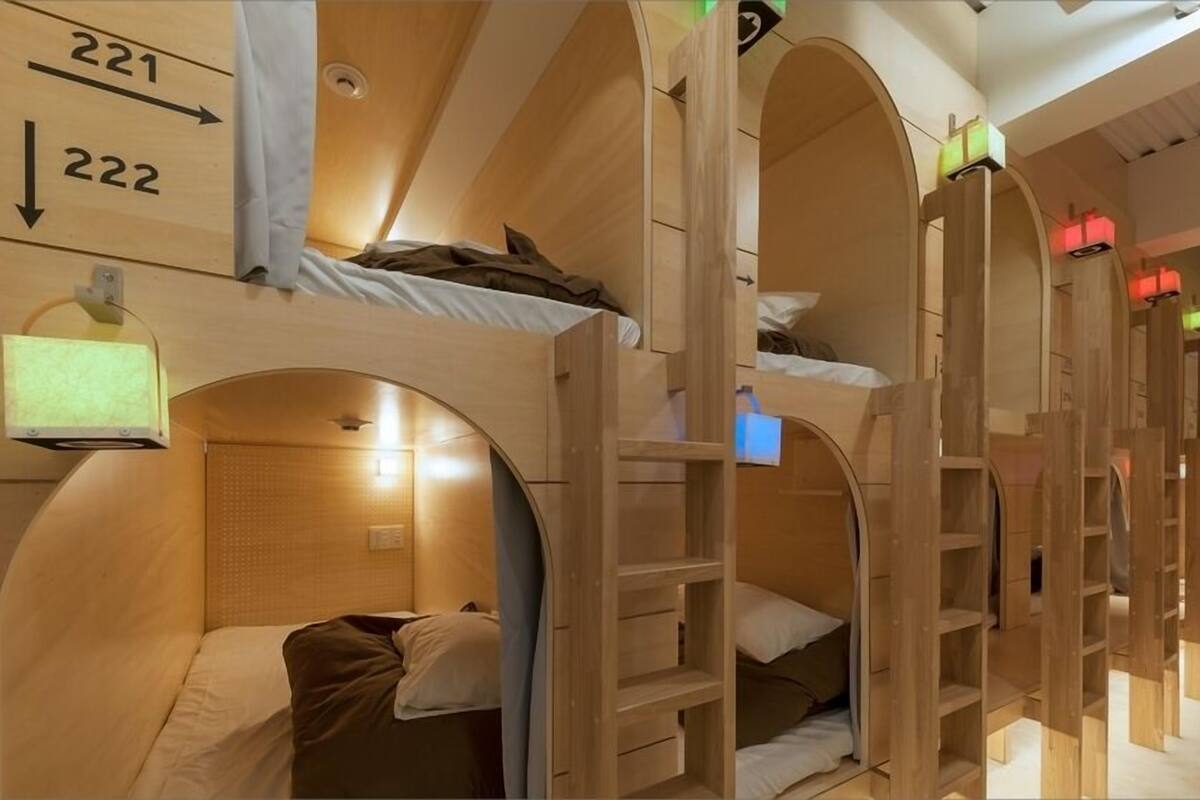 A row of bunk beds with wooden arches, a small shelf, and a wall-mounted light fixture.