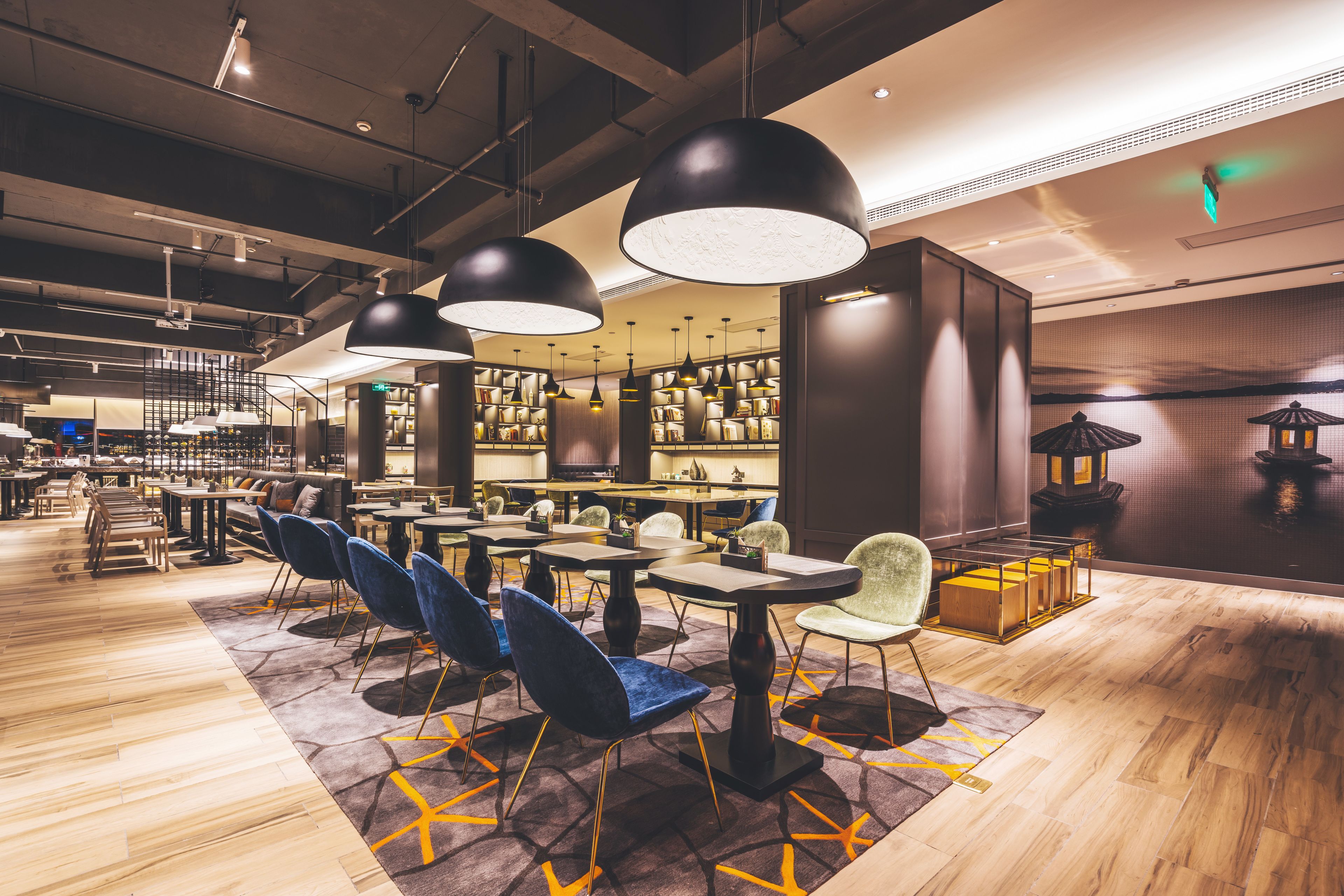 A modern hotel lobby with high ceilings, exposed beams, and a mix of seating areas including tables and chairs.