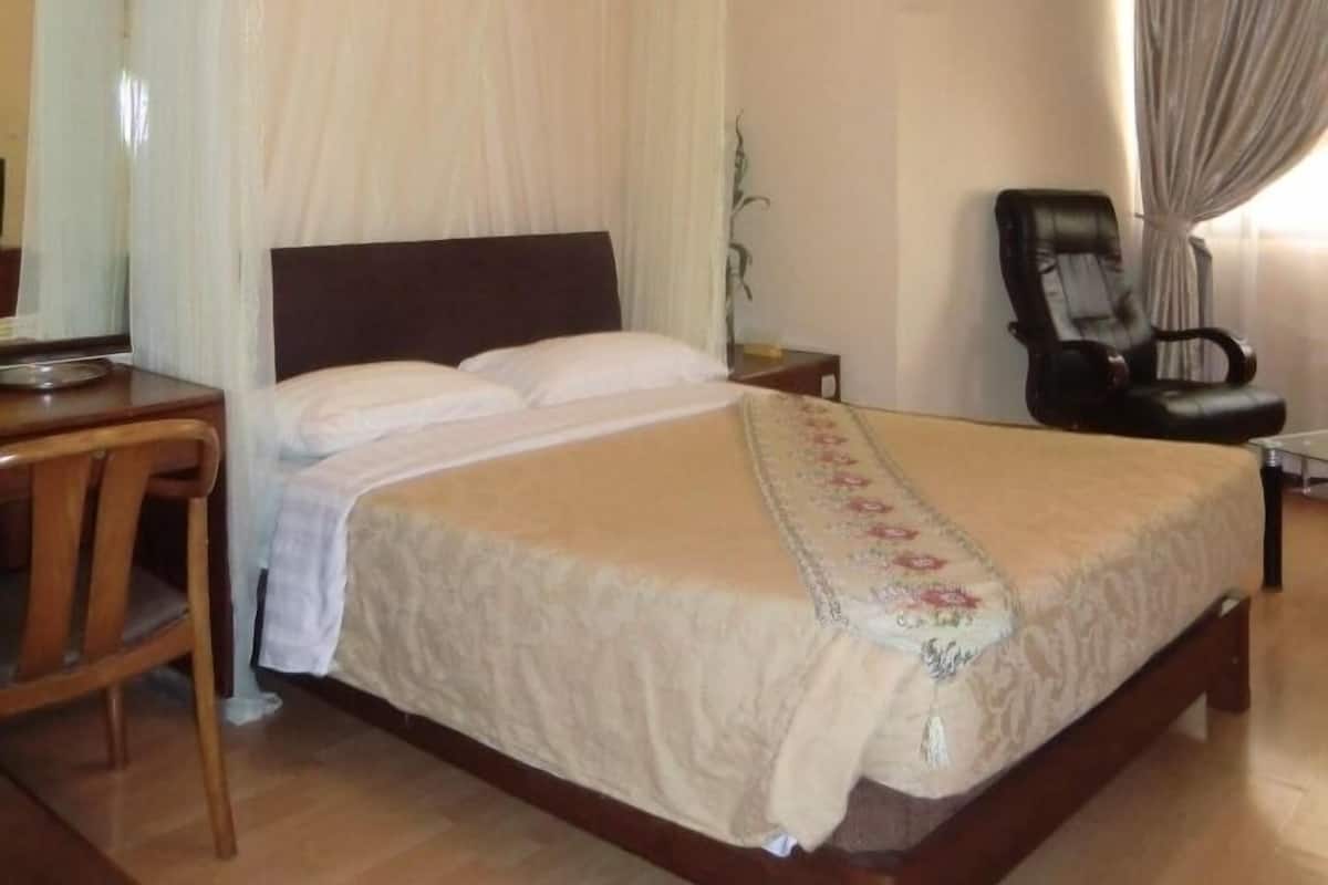 A four-poster bed with a canopy, a wooden desk, a chair, and a bedside table.