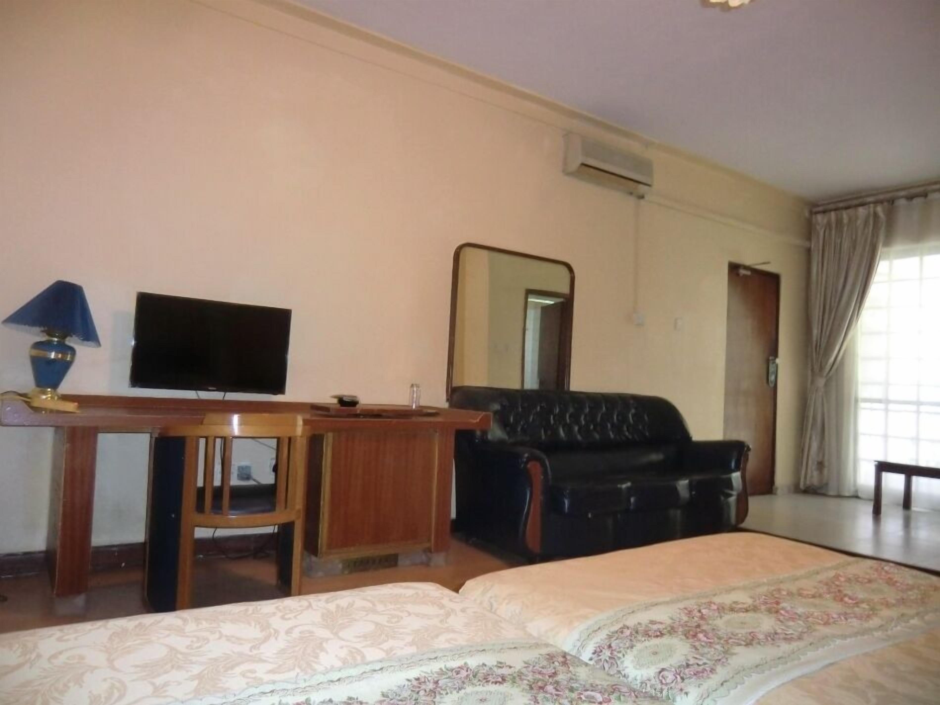 A hotel room with a bed, a desk, a television, a leather sofa, and a large mirror.