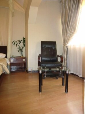 Una habitación con un sillón de cuero, una mesita de noche de madera, una mesa de vidrio y una planta en maceta.