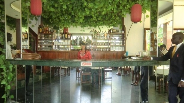 A bar area with a counter, shelves with bottles, and a person standing by the counter. - Fang Fang Hotel (Kampala)