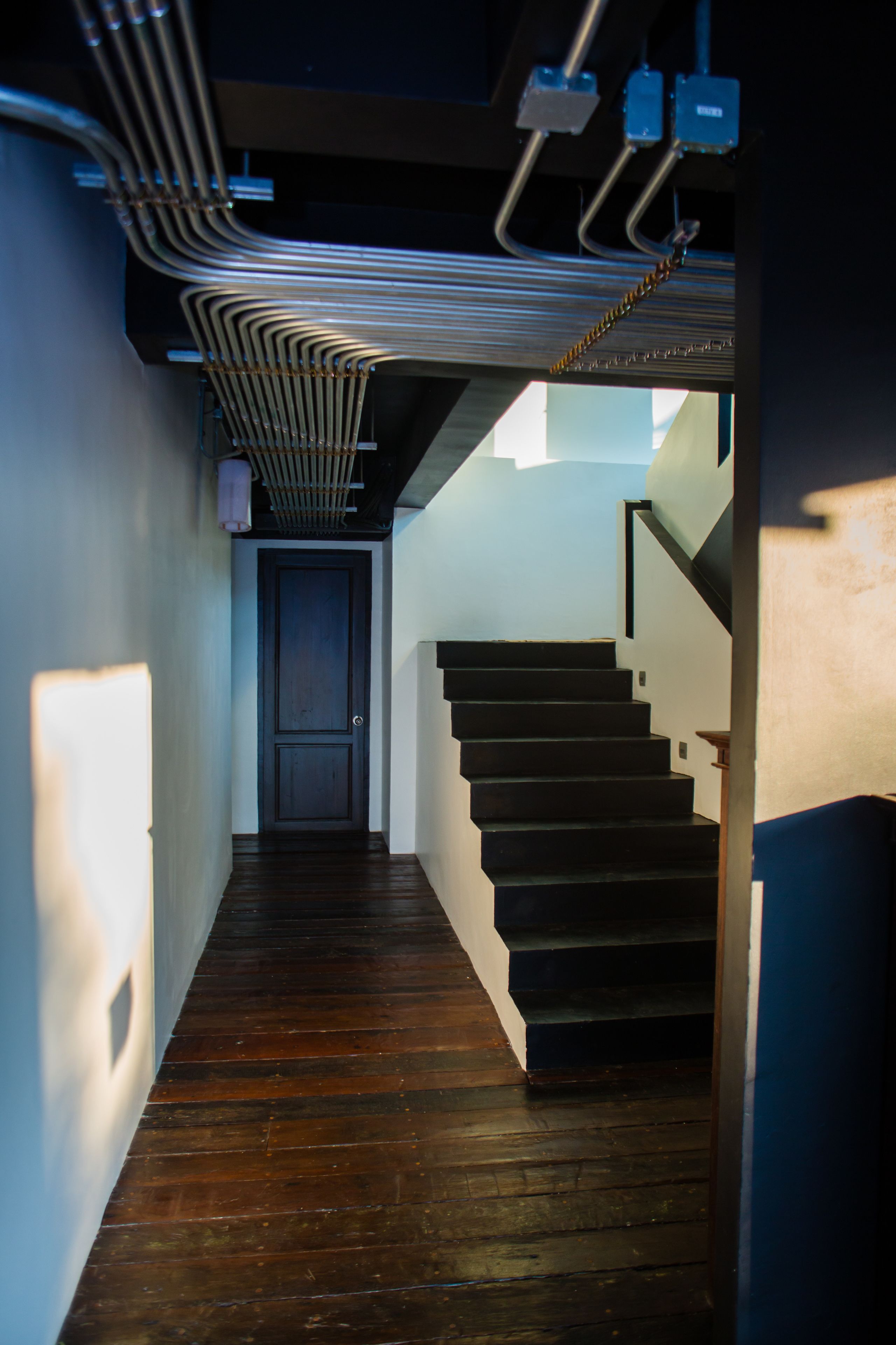 A narrow hallway with wooden flooring leading to a dark wooden staircase.