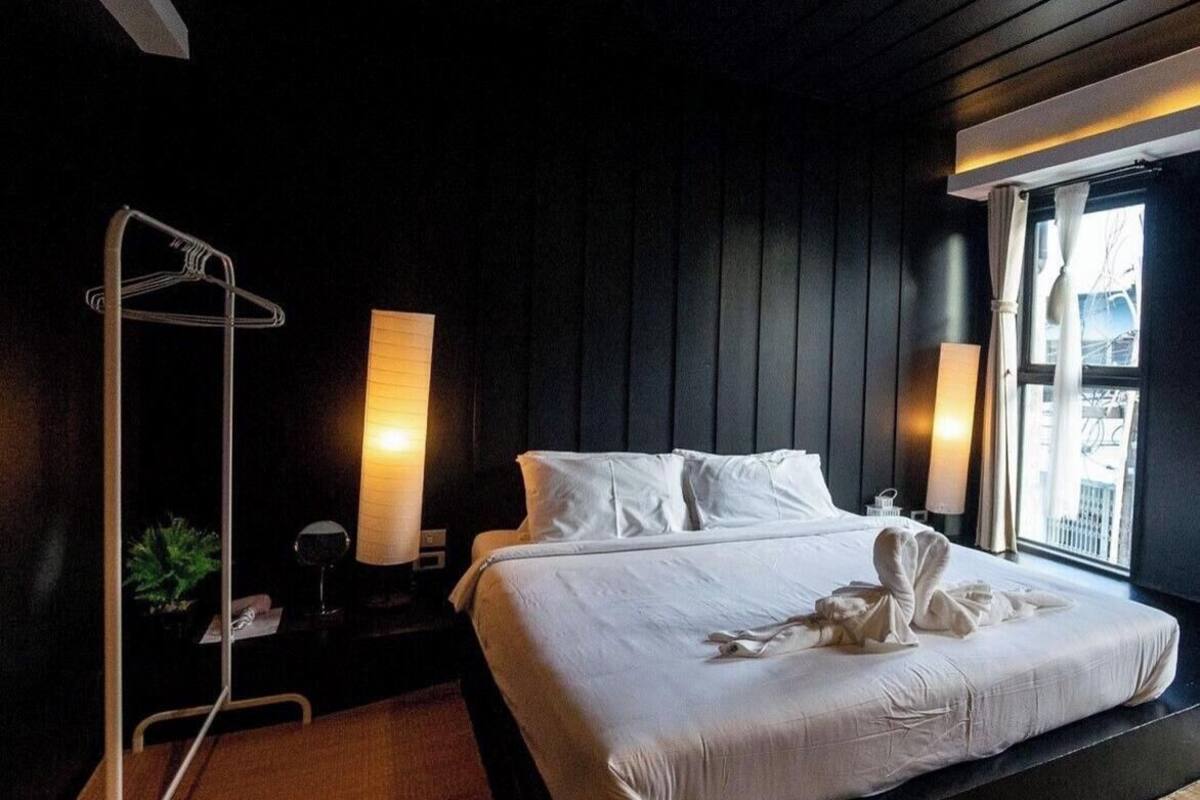 A hotel room with a bed, bedside lamps, a window with curtains, and a plant.