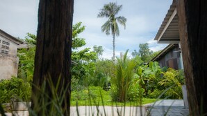 A lush garden with a tall palm tree, a concrete pathway, and a building with a sloped roof. - Trat 101 Hotel (Trat)