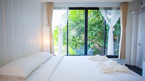 A hotel room with a large bed, a window with curtains, and a view of greenery outside. - Trat 101 Hotel (Trat)