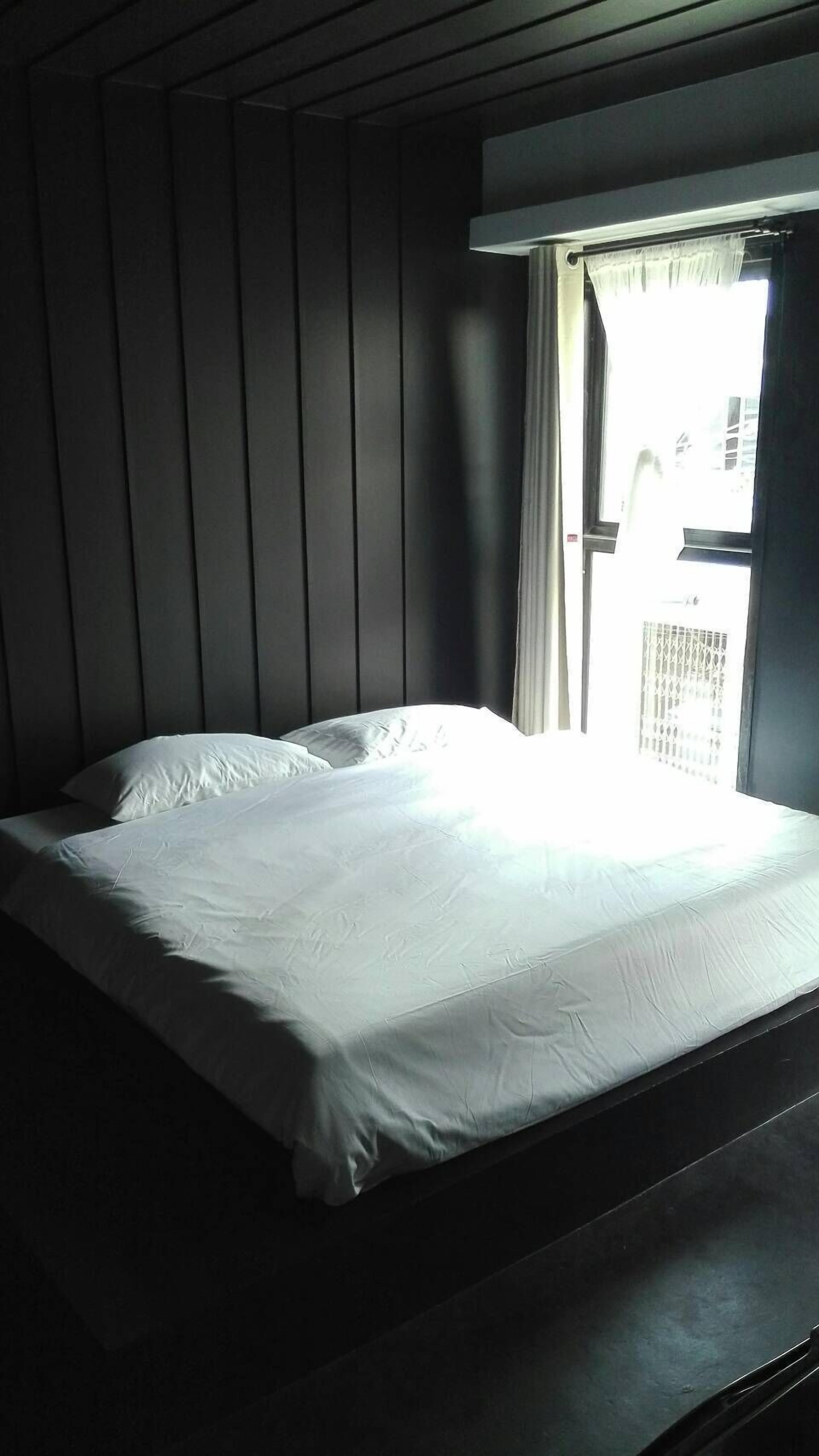 A single bed in a room with a window and a view of buildings outside.