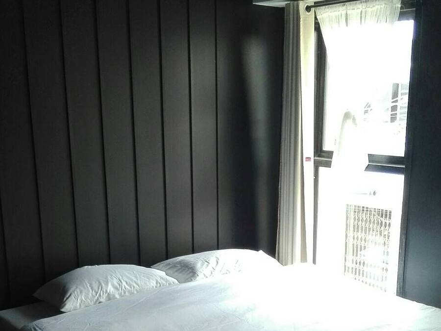 A single bed in a room with a window and a view of buildings outside.