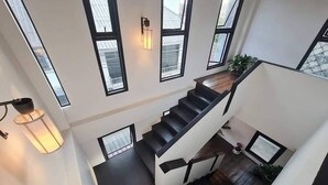A modern staircase with black steps and white walls, large windows, and a wall-mounted light fixture. - Trat 101 Hotel (Trat)
