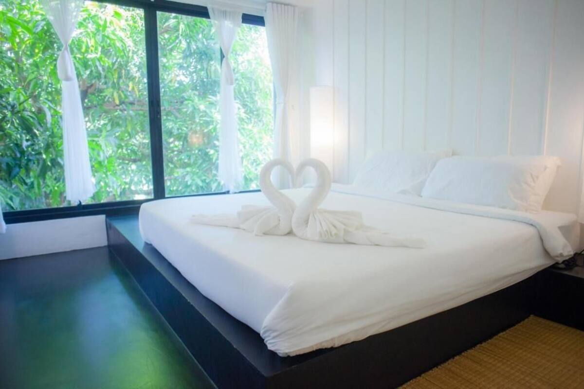 A hotel room with a bed, a window with curtains, and a view of greenery outside.