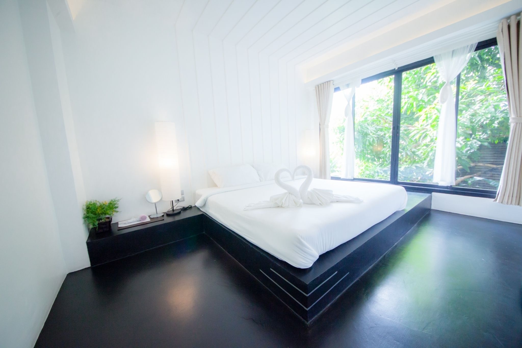Une chambre moderne avec un grand lit, une table de chevet avec une lampe et une fenêtre avec des rideaux.