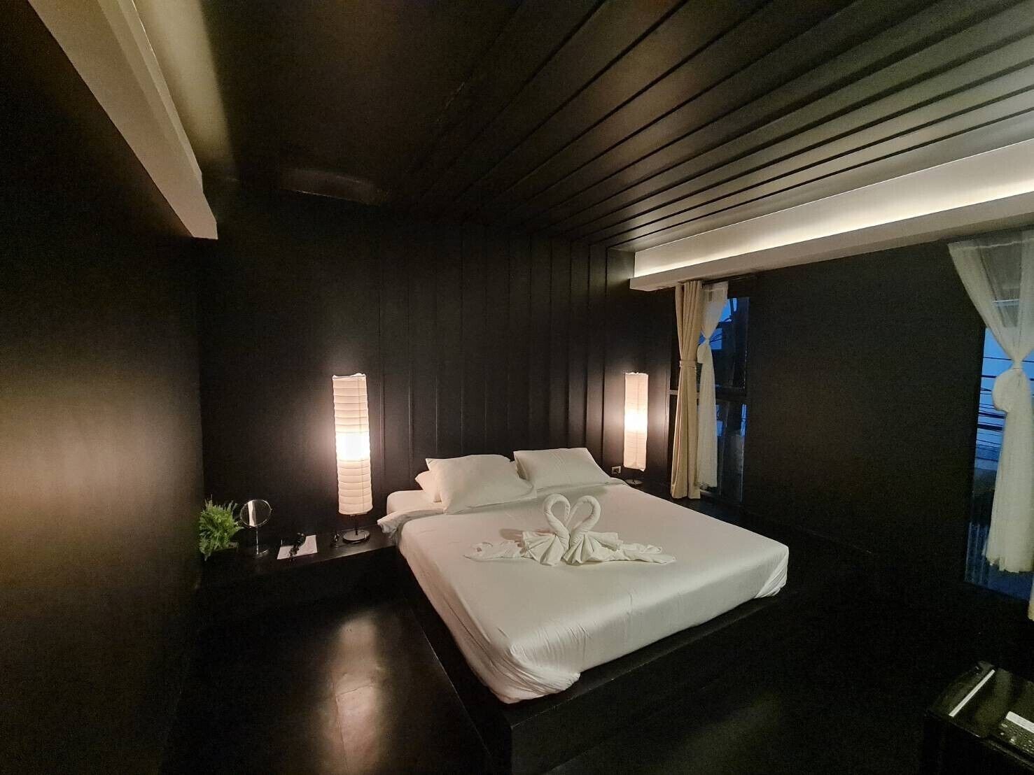 Une chambre d’hôtel avec un grand lit, deux lampes de chevet, une table de chevet et une fenêtre avec des rideaux.