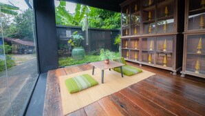 A room with a wooden floor, a table with a vase, green cushions, and a view of a garden with trees and a large window. - Trat 101 Hotel (Trat)
