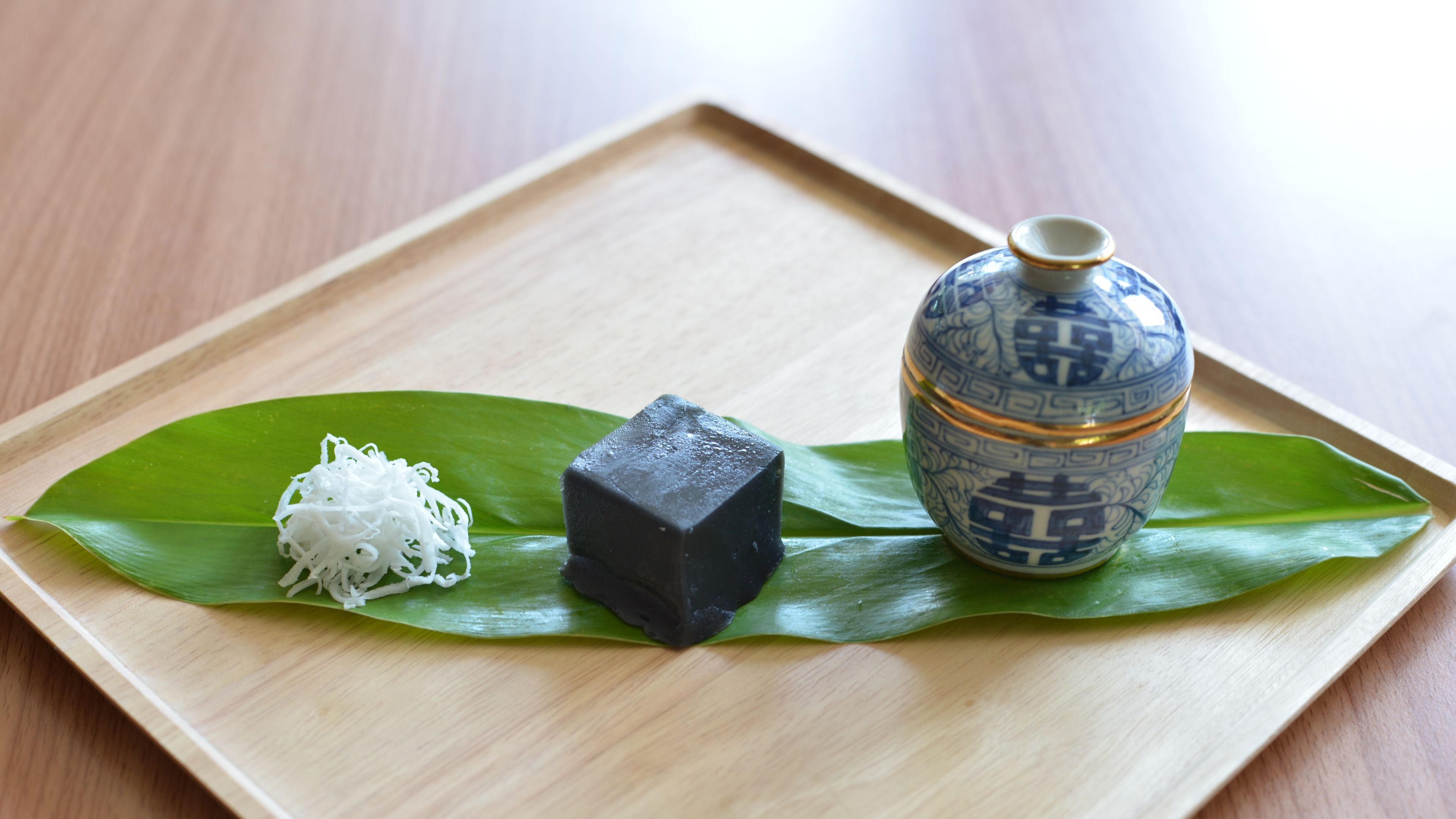 A wooden tray with a green leaf, a black cube, and a blue and white ceramic container.