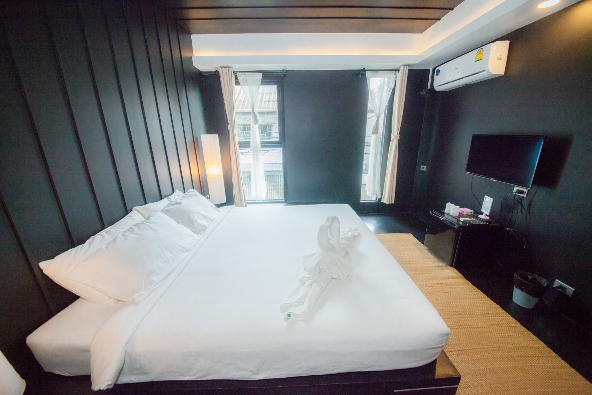 A hotel room with a neatly made bed, a flat-screen TV mounted on the wall, and a window with curtains.
